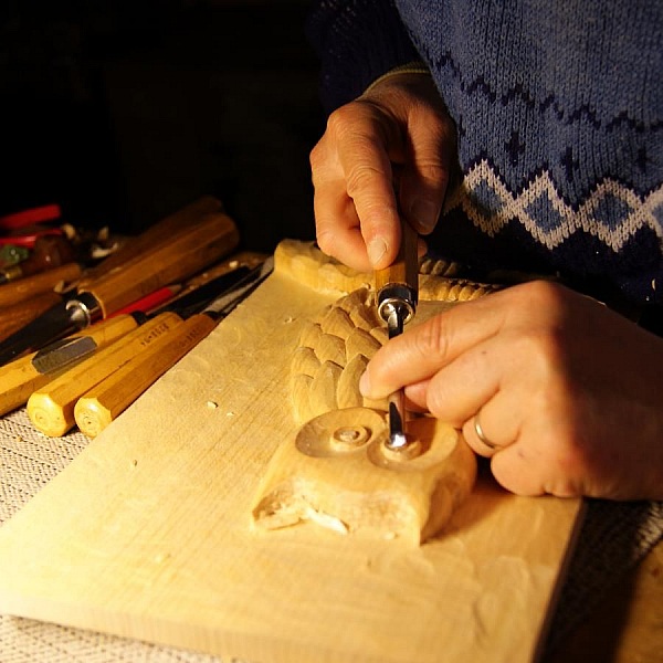 Artisan sculptant une chouette en bois avec un ciseau.