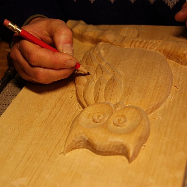 Artisan dessinant une chouette sculptée sur une planche bois.